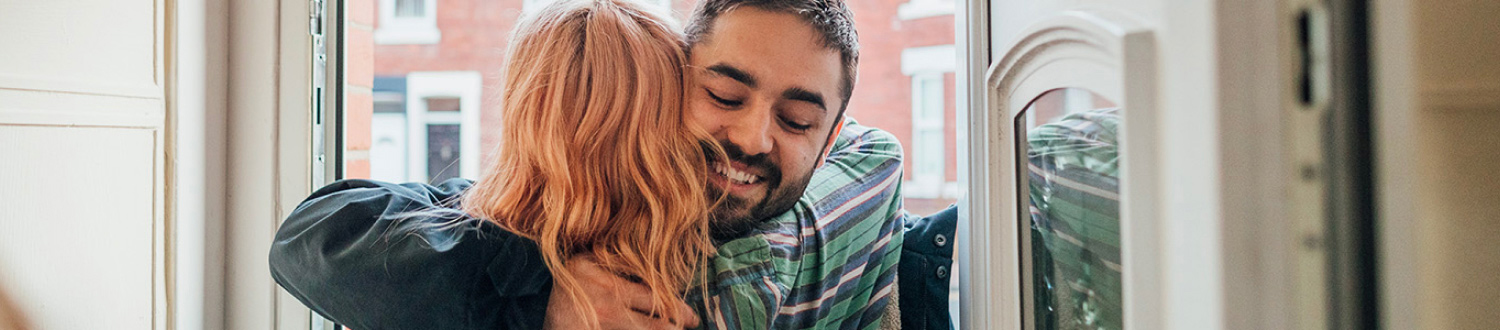 Two people hugging at the front door of a house