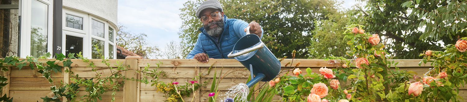 A person leaning over a fence to water plants