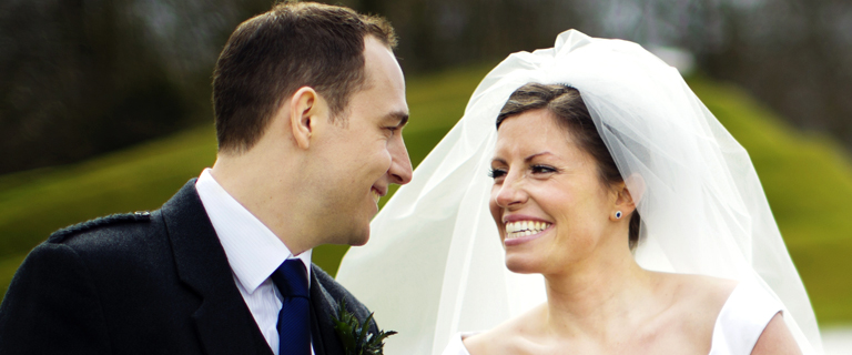 A bride and a person in a suit smiling at each other