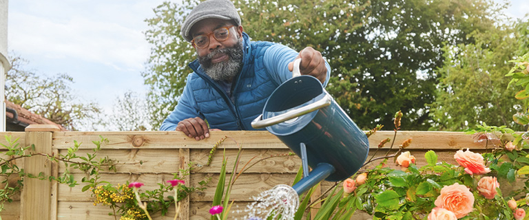 A person leaning over a fence to water plants