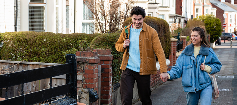 Two people holding hands, smiling and walking down the street