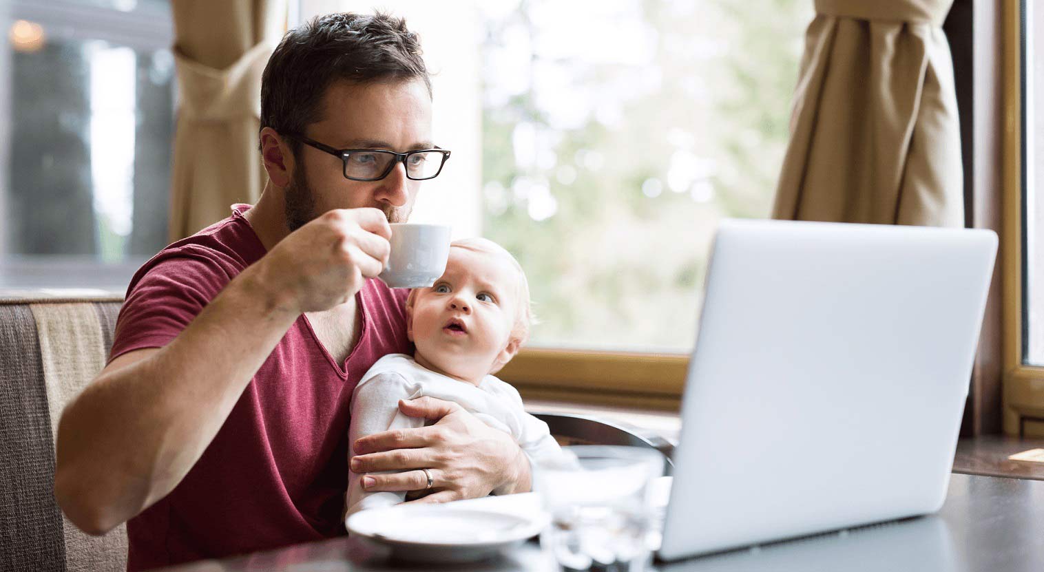 dad with baby at home looking at laptop