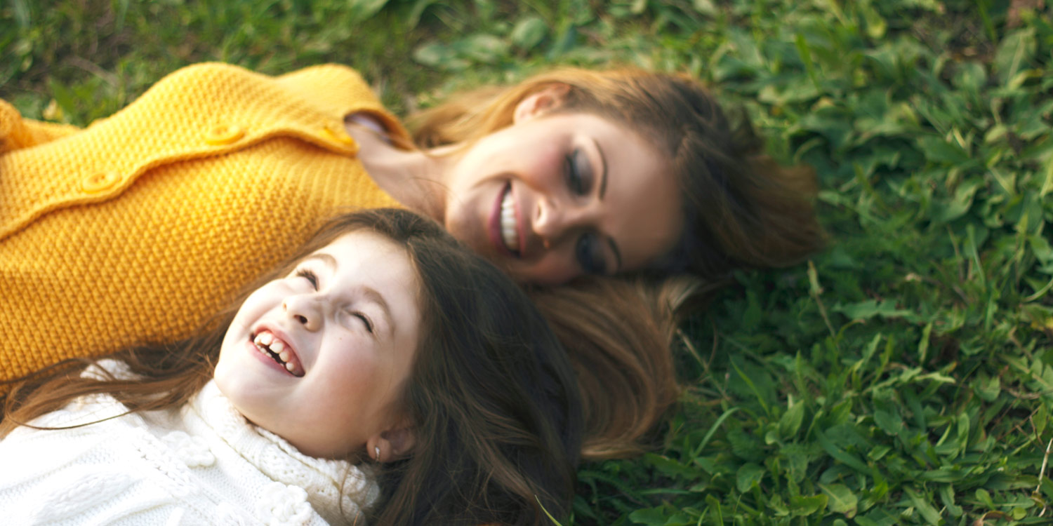 mother and daughter laying on grass together happy and smiling