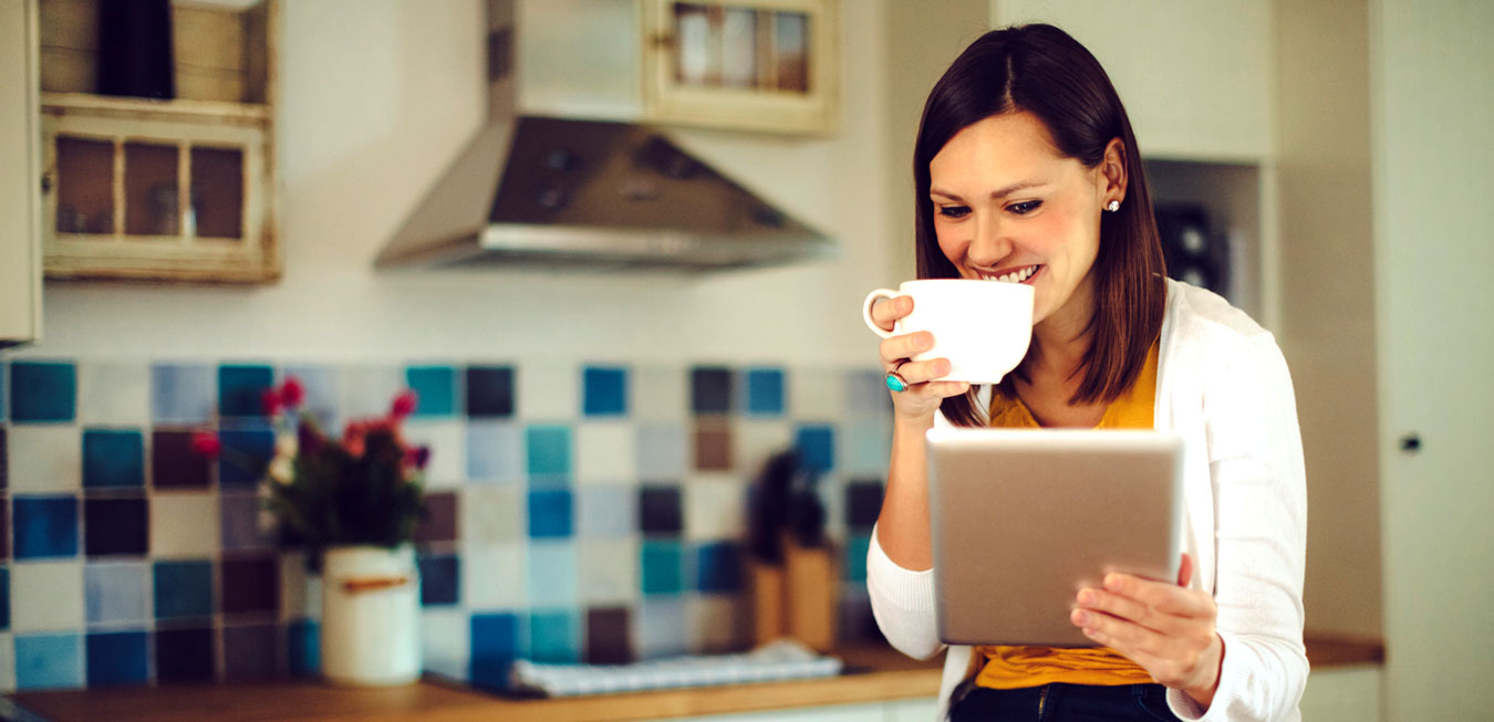woman drinking a cup of tea and looking at tablet