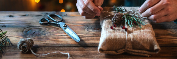 person wrapping a Christmas present in a linen sack on a hardwood table 