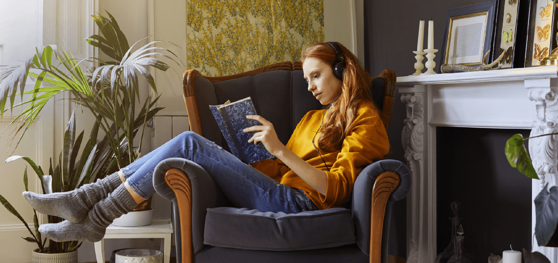 woman reading book whilst sitting in an armchair wearing headphones