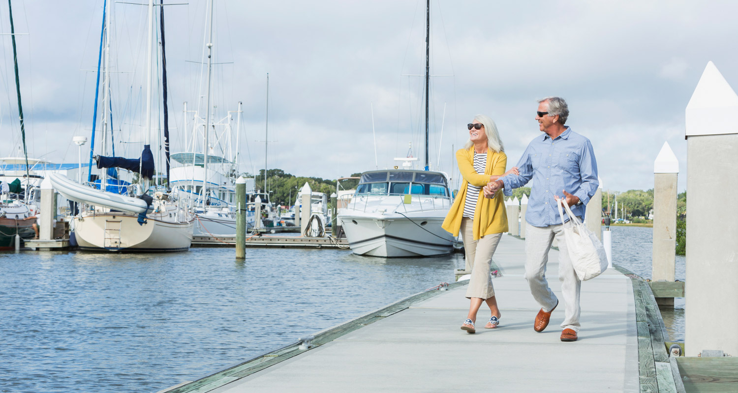 Two people walking by a harbour filled with boats