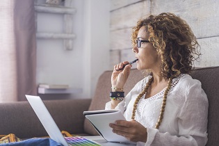 woman on laptop with a notepad and pen in her hands