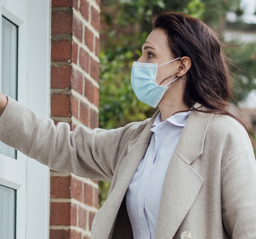 Woman wearing professional clothing and a face mask knocking on the front door of a house