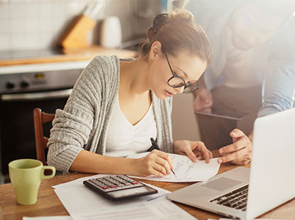 woman filling out paperwork with calculator & laptop