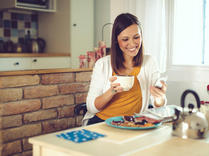 woman on phone holding a mug of tea in a kitchen